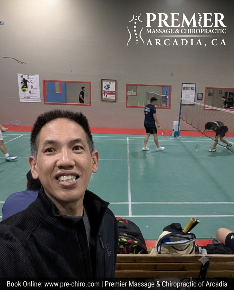 Dr. Kwan smiling broadly in the foreground of a bustling badminton facility