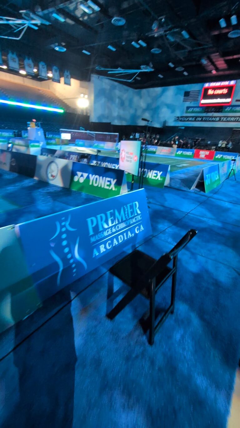 beautifully features the prominent A-frame sign reading "PREMIER MASSAGE & CHIROPRACTIC, ARCADIA, CA" directly in the foreground, with the court layout and the "Titan Gym" atmosphere softly blurred in the background.