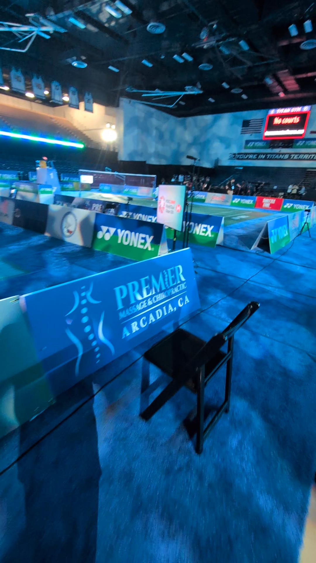 beautifully features the prominent A-frame sign reading "PREMIER MASSAGE & CHIROPRACTIC, ARCADIA, CA" directly in the foreground, with the court layout and the "Titan Gym" atmosphere softly blurred in the background.